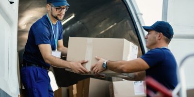 young couriers cooperating while unloading packages from deliver
