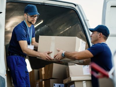 young couriers cooperating while unloading packages from deliver